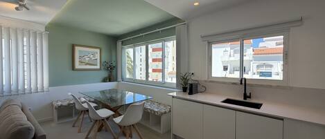 Una cocina moderna con una mesa de comedor de vidrio, armarios blancos y vistas de la ciudad a través de amplias ventanas.