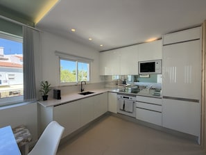 A modern kitchen with white cabinets, a built-in microwave, and a window with a view of the outside. - Central Town 2-bedroom Classy Apartment Albufeira (Albufeira)