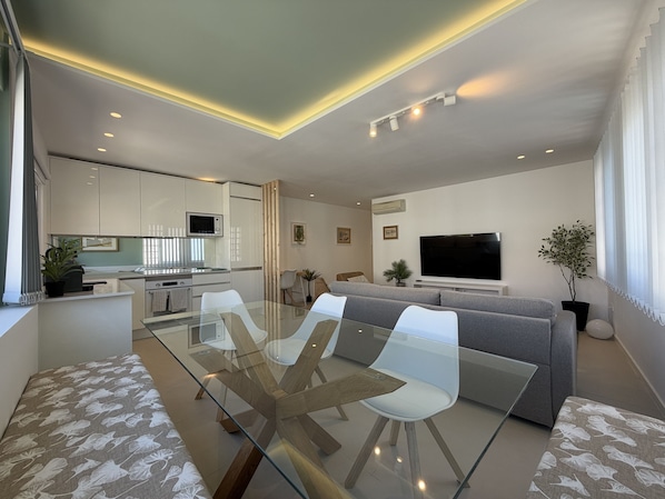 A modern living room with a glass dining table, grey sofa, and a flat-screen TV. - Central Town Classy T2 by Agarve Lodging (Albufeira)