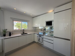 A modern kitchen with white cabinets, a built-in oven, and a window with a view of trees. - Central Town 2-bedroom Classy Apartment Albufeira (Albufeira)