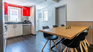 A modern kitchen with white cabinets, a red accent wall, and a built-in dishwasher. - Geneve Old Town T3 Apartment (Albufeira)