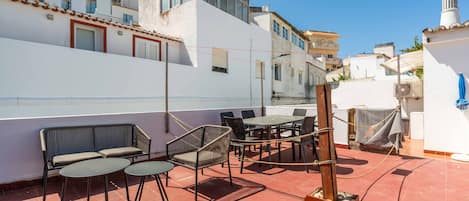 Une terrasse sur le toit avec un espace extérieur aménagé, comprenant des tables et des chaises, ainsi qu’un foyer.