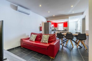 Ein modernes Wohnzimmer mit einem roten Sofa, schwarzen Stühlen und einer Küche im Hintergrund.