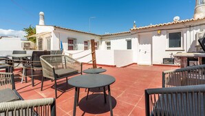 A rooftop terrace with outdoor seating, a white building with a chimney, and a clear blue sky. - Geneve Old Town T3 Apartment (Albufeira)