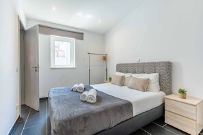 Ein modernes Schlafzimmer mit einem großen Bett, einem Nachttisch, einem Fenster und einer Tür.