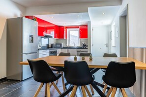 A modern kitchen with a dining area, featuring a large wooden table, black chairs, and red cabinetry. - Geneve Old Town T3 Apartment (Albufeira)