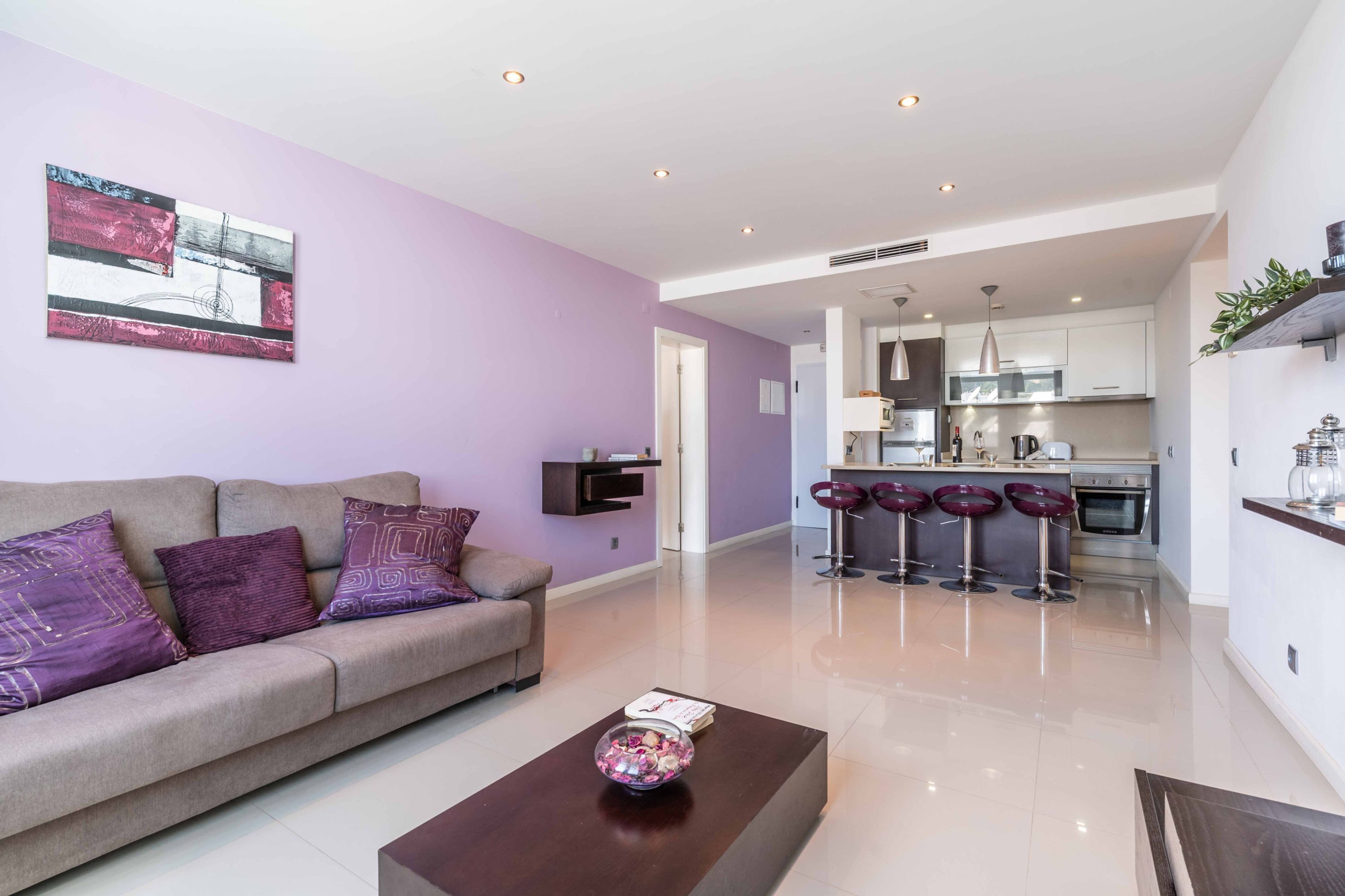 A modern living room with a sofa, coffee table, and a kitchen in the background.