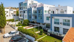 Um edifício residencial moderno de vários andares com varandas, entrada pavimentada e carros estacionados.