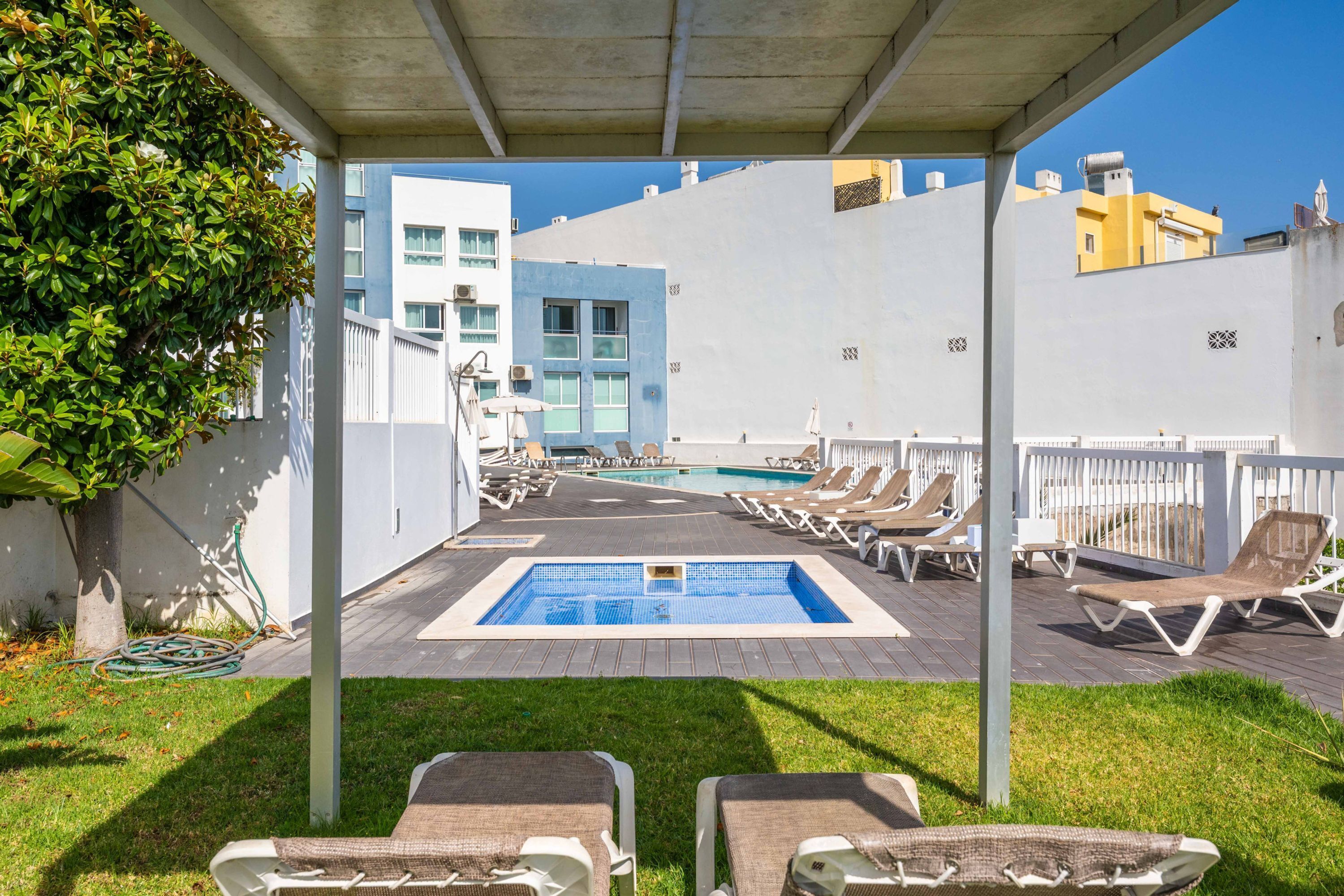 Un área de piscina en la azotea con sillones reclinables y una piscina pequeña.