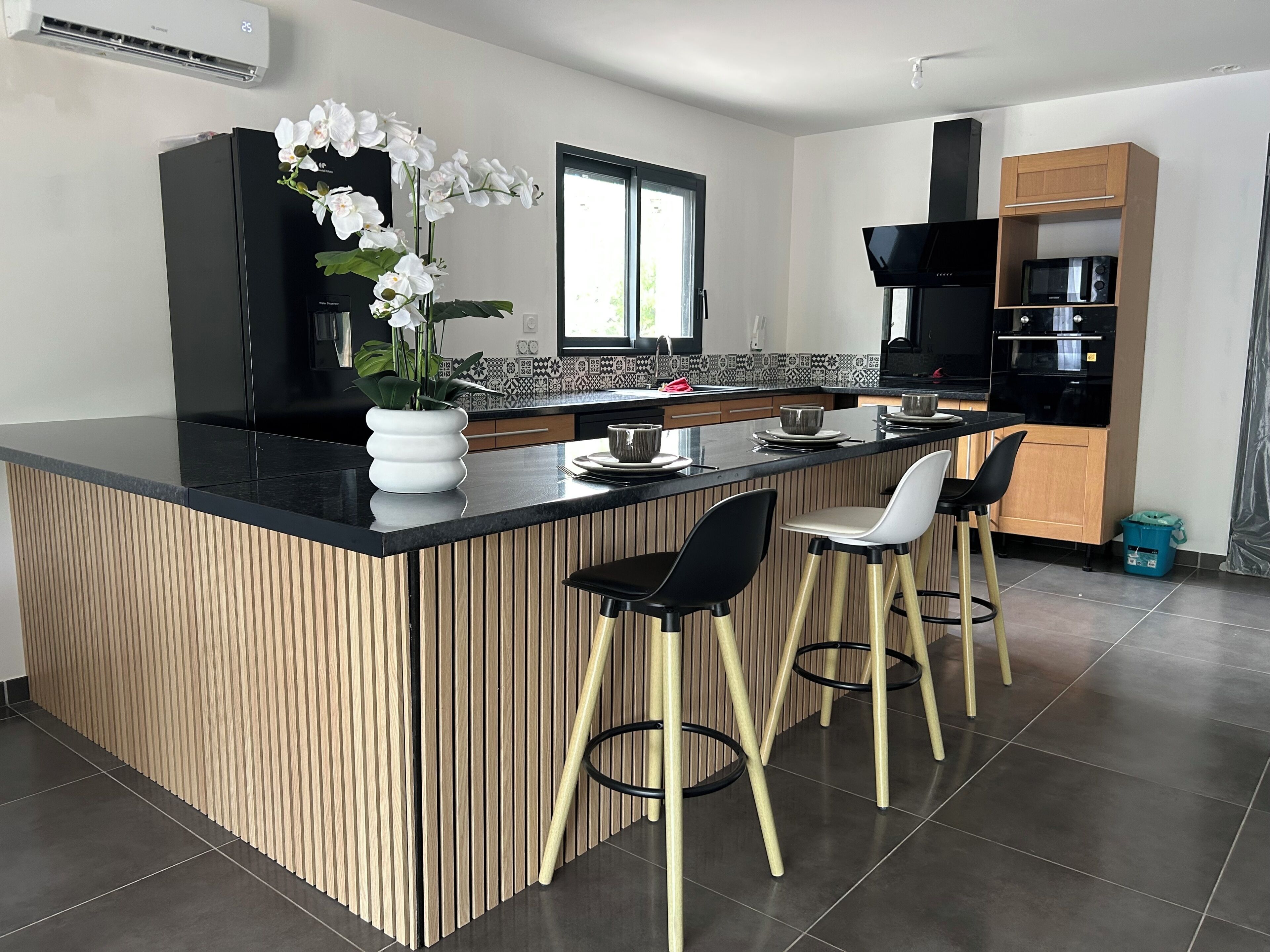 A modern kitchen with a central island, bar stools, a microwave, and a black range hood.