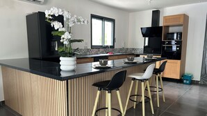 A modern kitchen with a central island, bar stools, a microwave, and a black range hood.