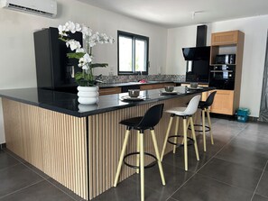 A modern kitchen with a central island, bar stools, a microwave, and a black range hood.