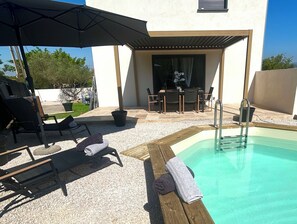 A poolside area with a sun lounger, a table, and a grill.