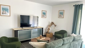 Un soggiorno con televisore a schermo piatto, arredamento imbottito verde, un tavolino in legno e opere d'arte incorniciate alle pareti.