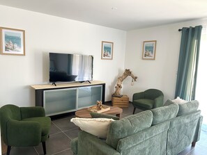 A living room with a flat-screen TV, green upholstered furniture, a wooden coffee table, and framed artwork on the walls.