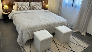 A modern bedroom with a large bed, two bedside lamps, a wooden headboard, and a view of the outdoors through sheer curtains.