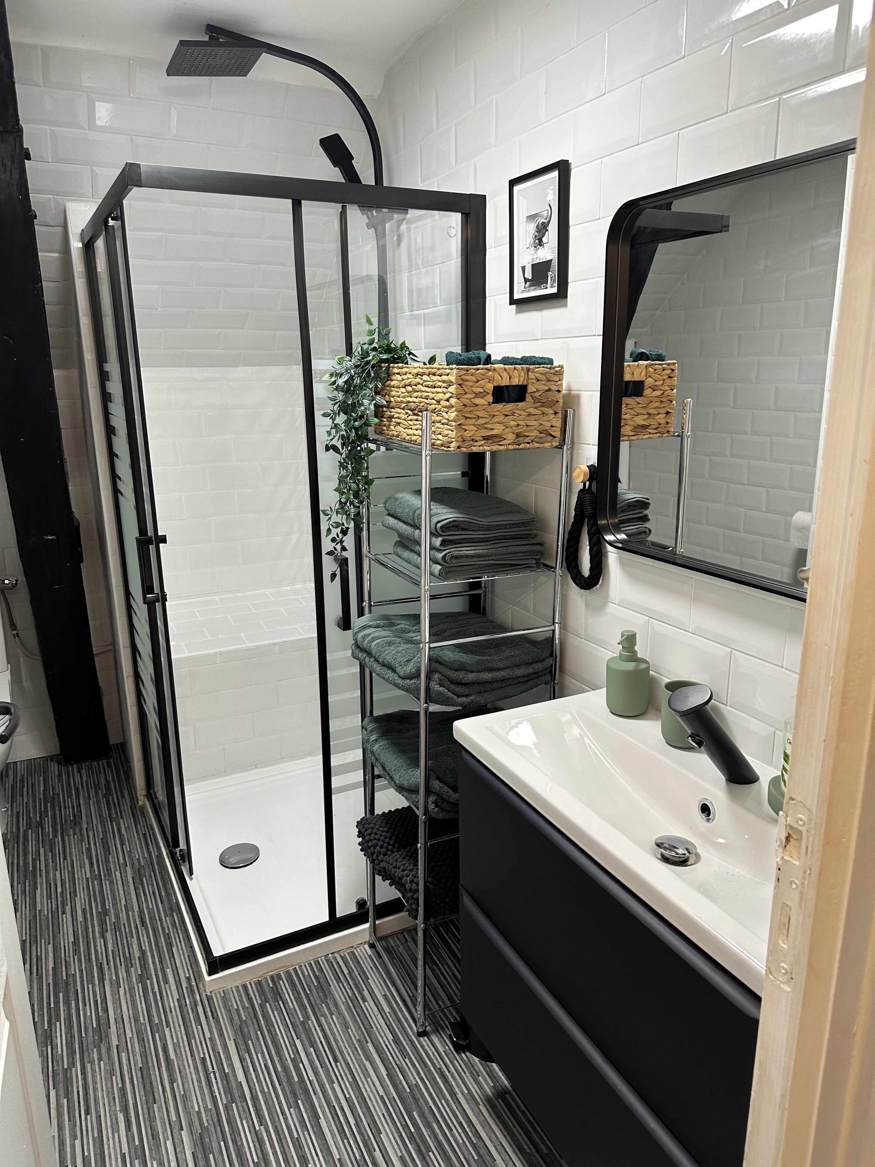 Une salle de bain moderne avec une douche à parois de verre, un lavabo blanc doté d’un robinet noir et un miroir au-dessus du lavabo.