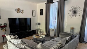 Una sala moderna con un televisor de pantalla plana grande, un sofá gris con cojines estampados, una mesita de centro redonda y un elemento decorativo en la pared.