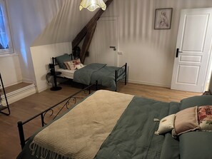 A room with two beds, a wooden staircase, a white door, and a framed picture on the wall. - Located in the heart of the village, at the foot of the Château de Bonneval. (Coussac-Bonneval)