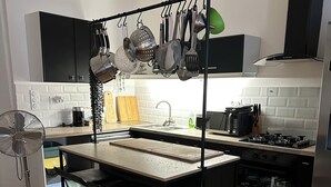 Una cocina moderna con una isla central, armarios negros, una suspensión para ollas y un horno empotrado.