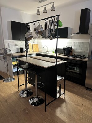 Eine moderne Küche mit einer zentralen Kochinsel, schwarzen Schränken, einer hängenden Pfannenträger und einem eingebauten Backofen.