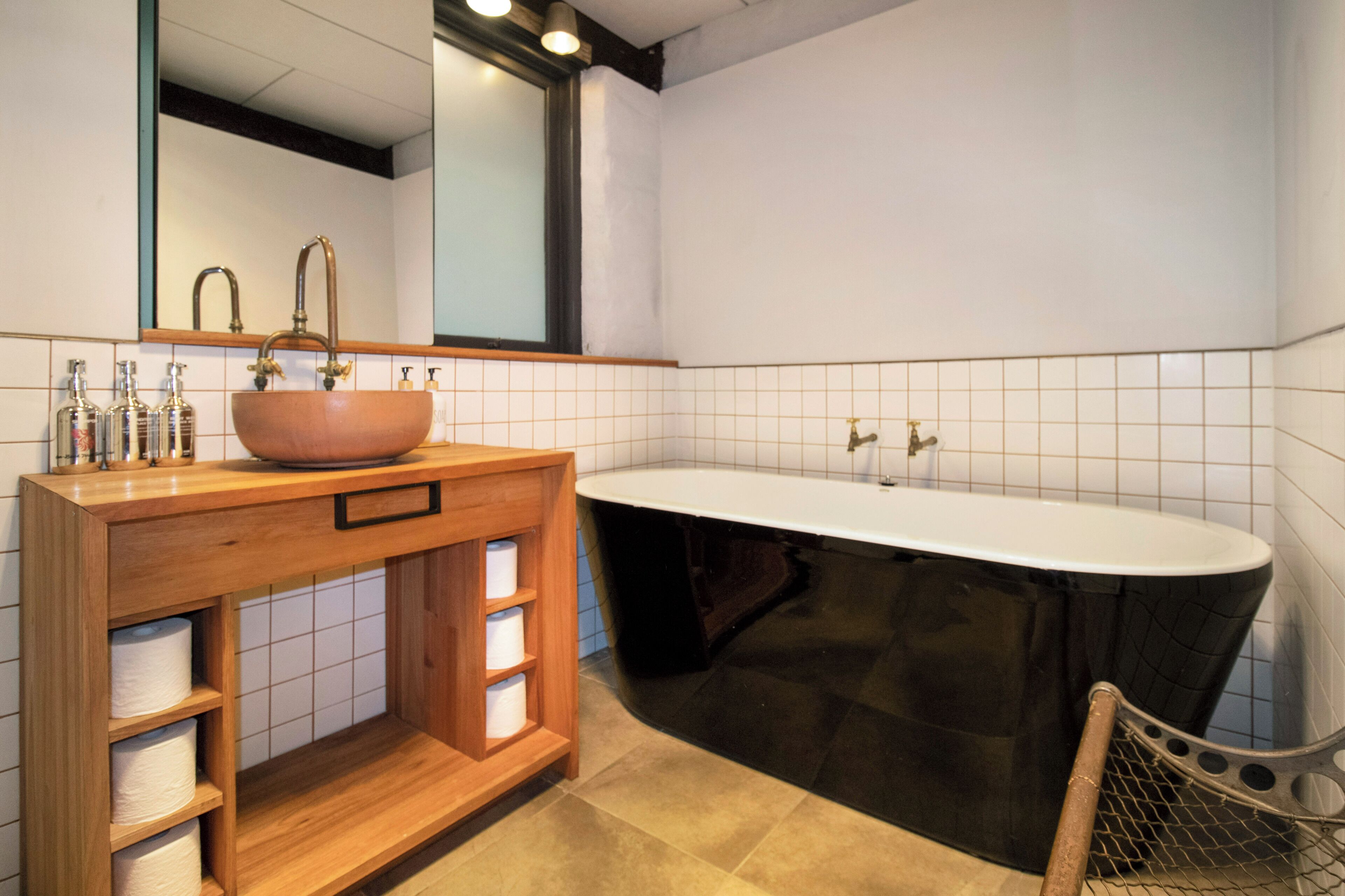A bathroom with a wooden vanity, a large oval sink, and a black bathtub.