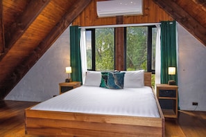 Ein Schlafzimmer mit einem hölzernen Bett, zwei Nachttischen, einem Fenster mit Vorhängen und einer Klimaanlage.