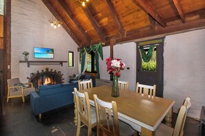Ein gemütliches Wohnzimmer mit Kamin, einem blauen Sofa, einem Esstisch mit Stühlen und einem an der Wand befestigten Fernseher.