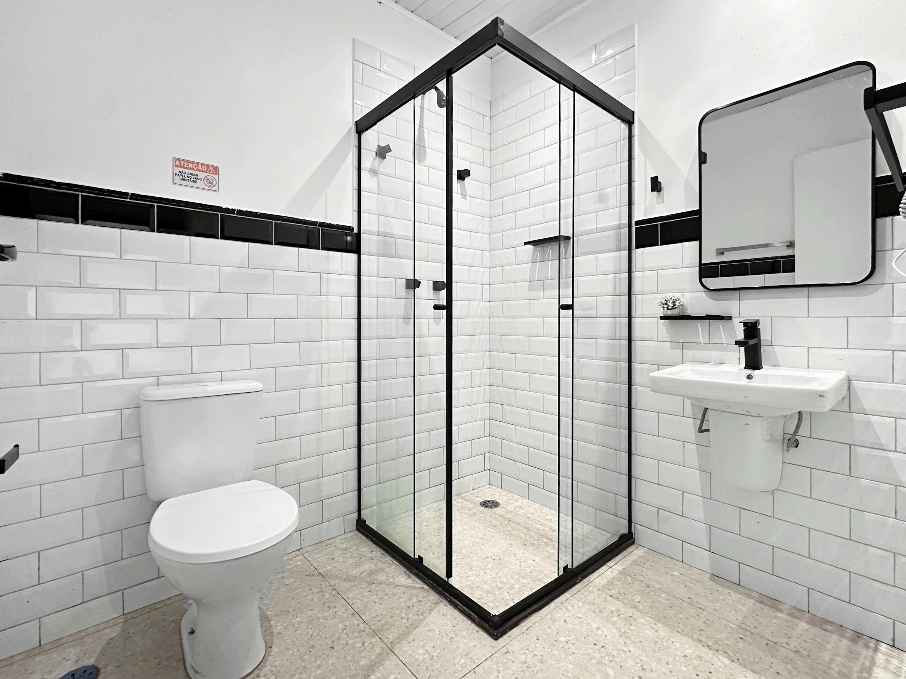 Uma casa de banho moderna com azulejos brancos tipo metrô, chuveiro com cabine de vidro, sanita branca e lavatório com espelho.
