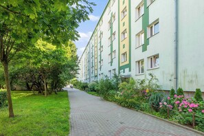 Ein Weg führt zu einem mehrstöckigen Gebäude mit grüner und weißer Fassade, umgeben von üppiger Vegetation und blühenden Pflanzen.