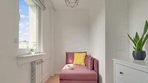 Habitación pequeña con un sofá rosa, una mesita con una taza y una bandeja, un radiador, una ventana con vistas y una planta en maceta.