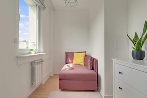 Ein gemütlicher Raum mit rosa Sofa, einem kleinen Tisch mit Tasse und Tablett, Heizkörper, Fenster mit Aussicht und einer Topfpflanze.