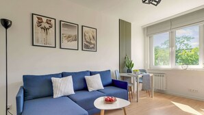 Una sala de estar moderna con un sofá azul, una mesita redonda y un ventanal con vistas a árboles.
