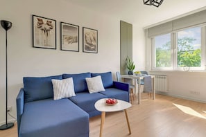 Ein modernes Wohnzimmer mit einem blauen Sofa, einem kleinen runden Tisch und einem Fenster mit Blick auf Bäume.