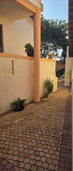 A paved courtyard with potted plants and a column. - Aloe Self Catering Two Bedroom Apartment Open Plan (Port Shepstone)
