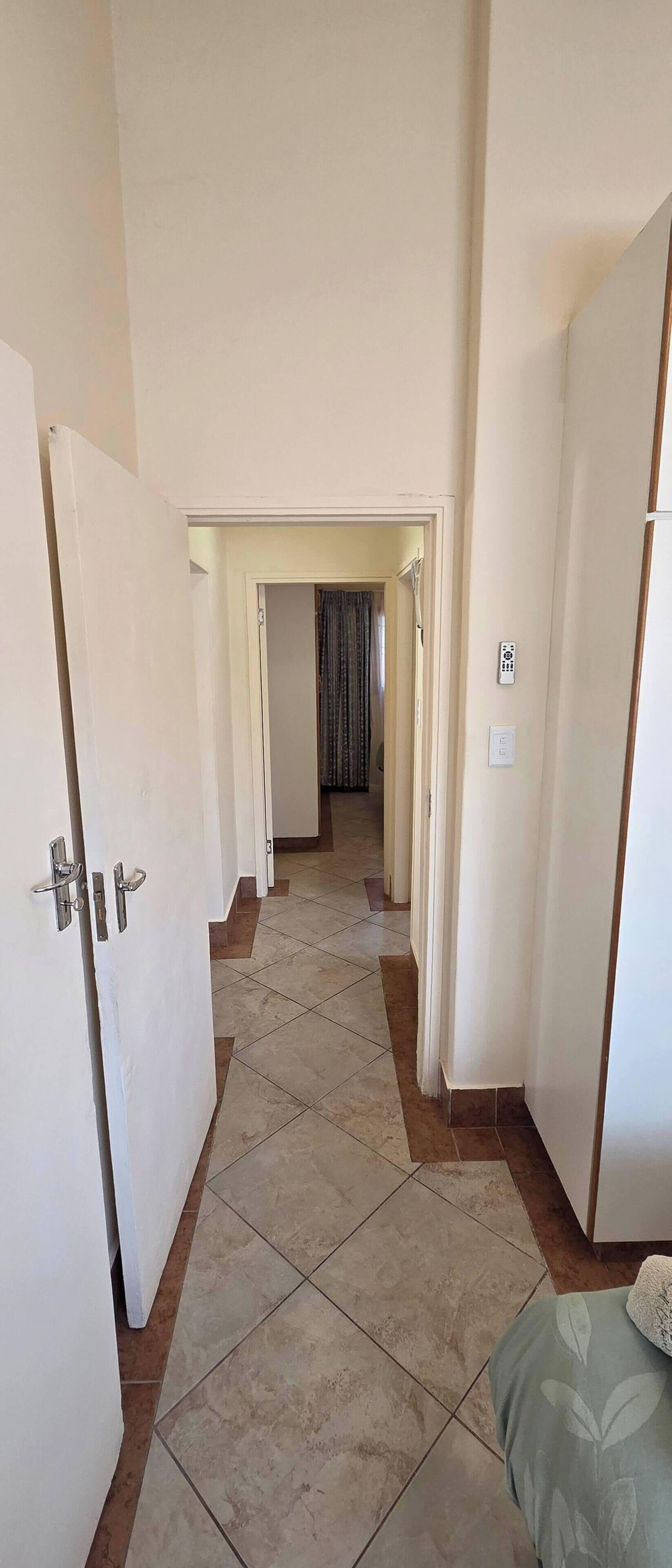Um corredor com portas que dão para quartos, chão ladrilhado e uma cama com cobertura estampada.