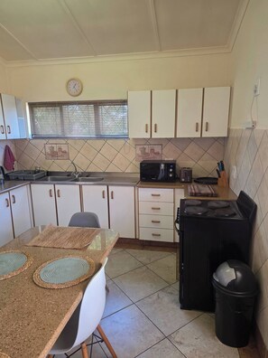A compact kitchen with white cabinets, a microwave, a stove, and a sink. - Aloe Self Catering Two Bedroom Apartment Open Plan (Port Shepstone)