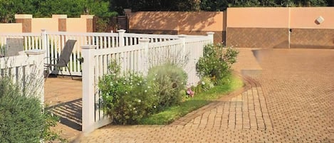 A paved outdoor area with a white fence, a tree, and a brick pathway.