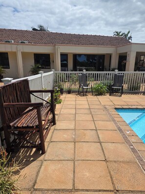 A poolside area with a tiled patio, two chairs, and a white fence. - Aloe Self Catering Two Bedroom Apartment Open Plan (Port Shepstone)