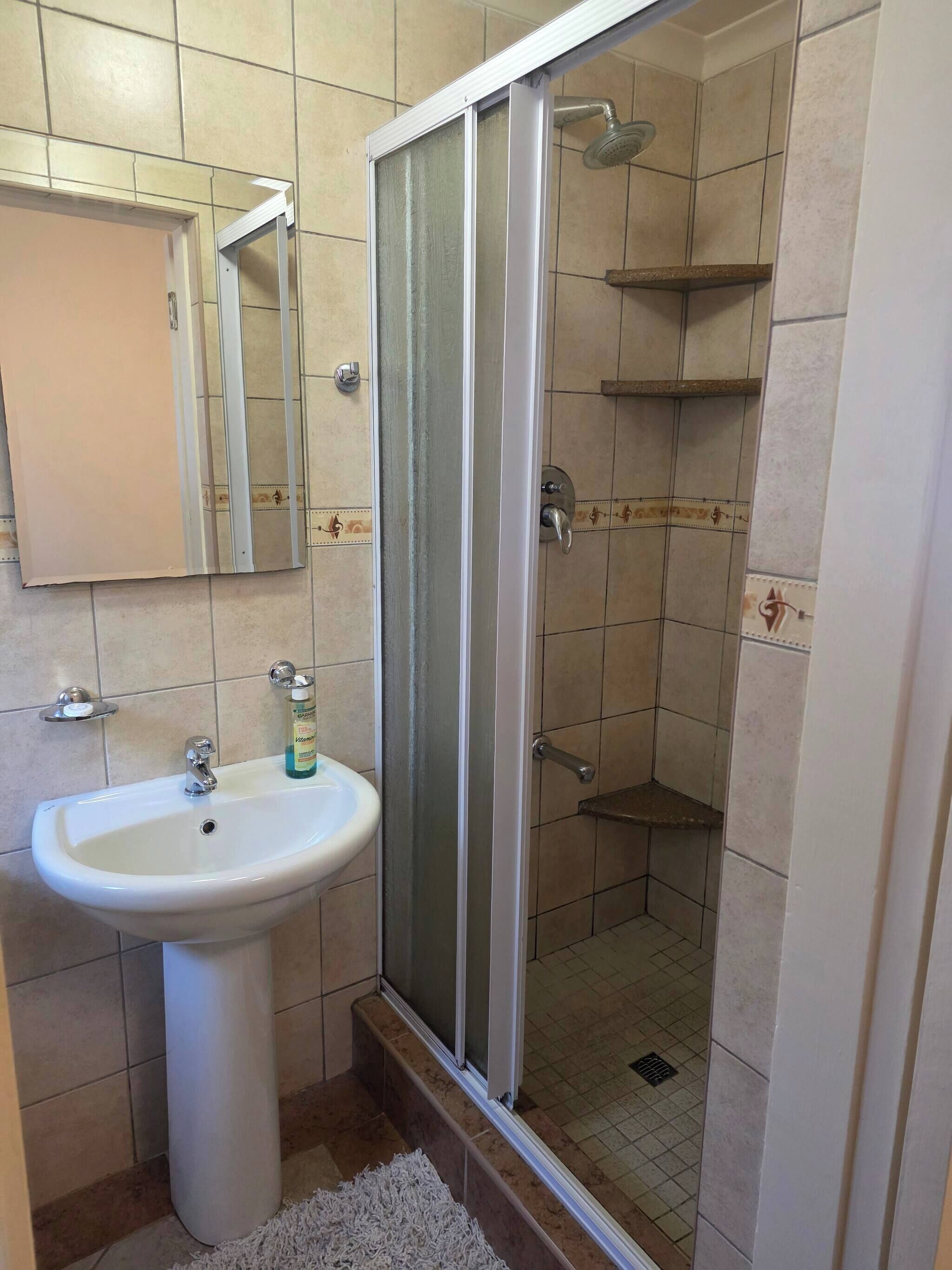 A bathroom with a white sink, a mirror, and a glass-enclosed shower.