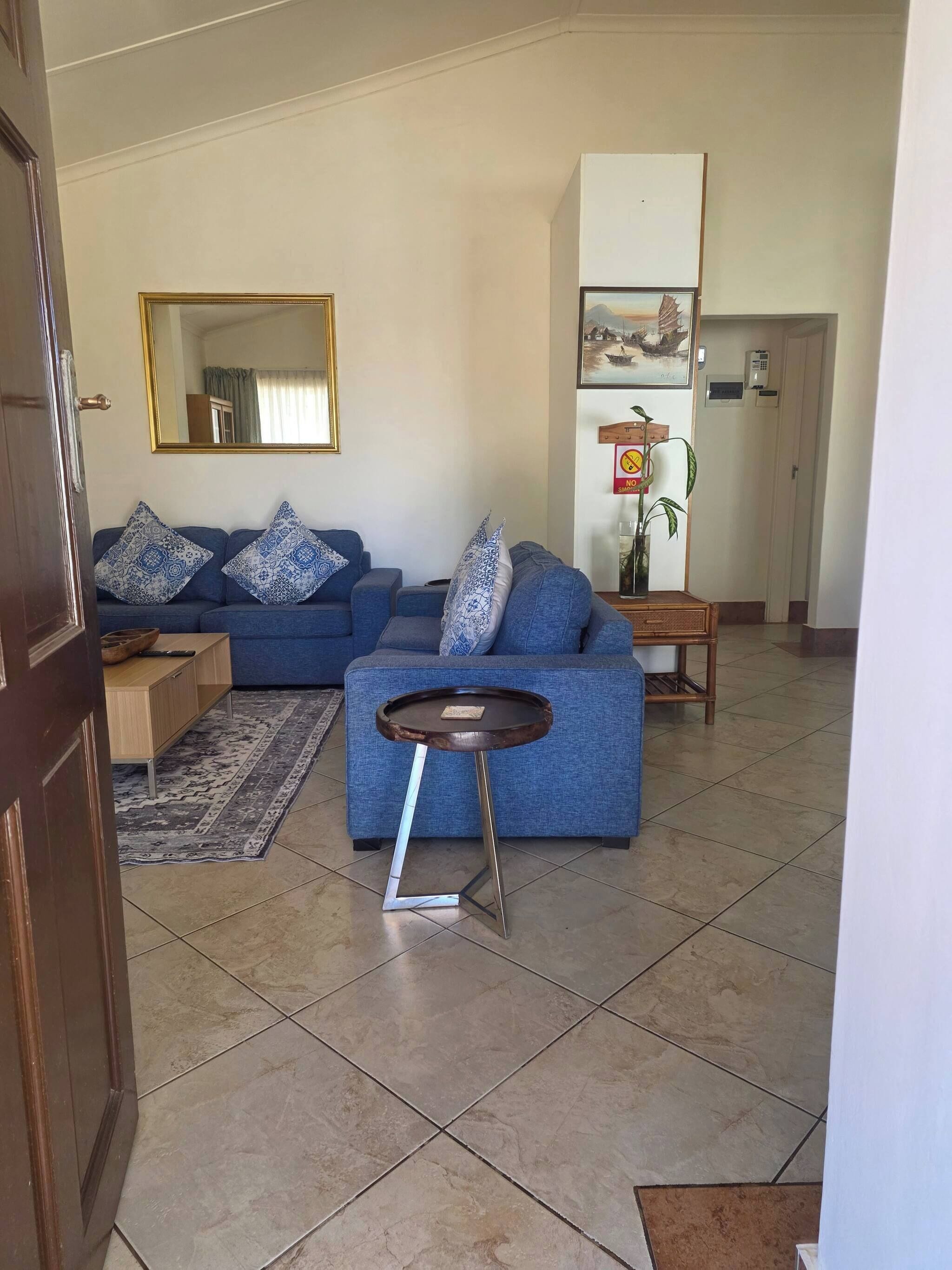 Una sala de estar con un sofá azul, una mesa redonda pequeña y un espejo en la pared.