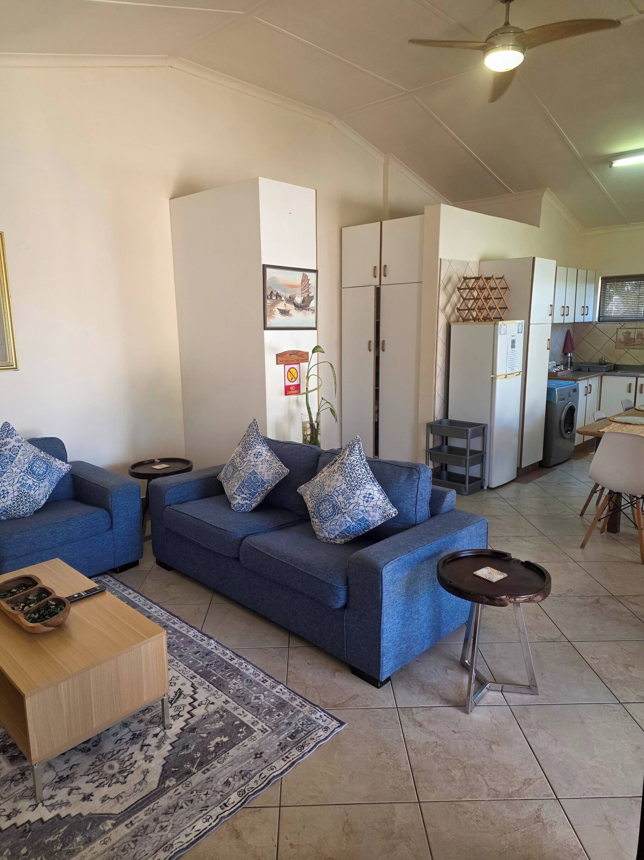 Uma sala de estar com sofá azul, mesa de centro, tapete e ventilador de teto.