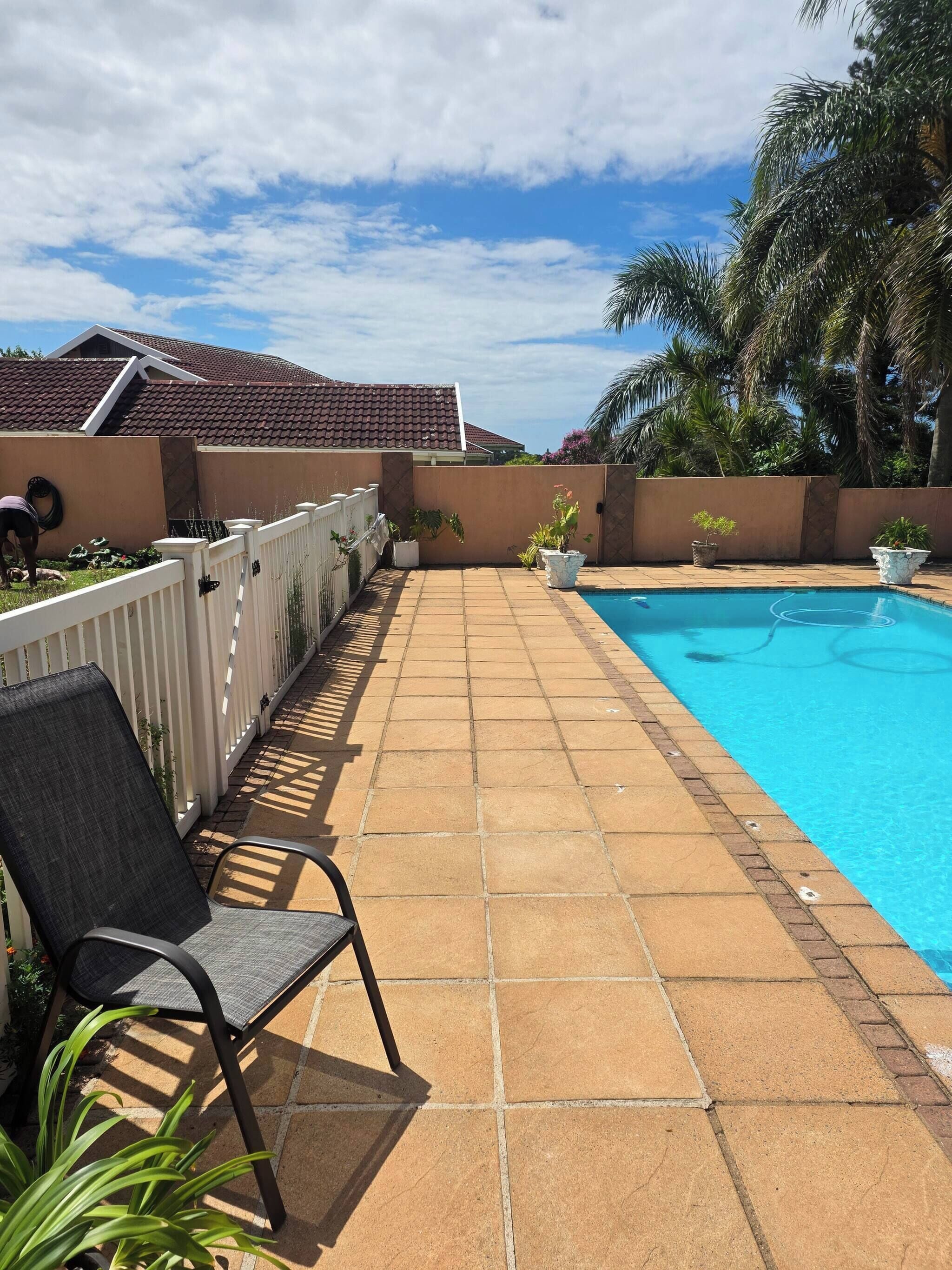 A swimming pool with a tiled deck, a chair, and a fence.