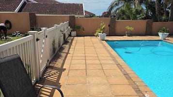 Una piscina con plataforma de baldosas, una silla y una valla.