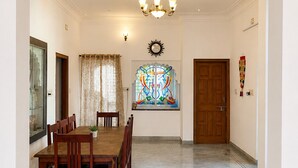 A dining room with a wooden table and chairs, a chandelier, a ceiling fan, and a stained glass window. - 3BHK Homestay in Udaipur, Lake View Private Terrace & Parking (Udaipur)