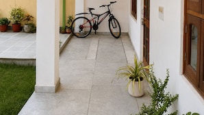 A covered outdoor area with a bicycle, potted plants, and a wall-mounted light fixture. - 3BHK Homestay in Udaipur, Lake View Private Terrace & Parking (Udaipur)