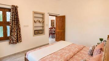 Un dormitorio con cama, ventilador de techo, ventana con cortinas y puerta que da a otra habitación.