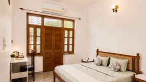 A bedroom with a bed, a desk, a chair, a ceiling fan, and a window with a wooden door. - 3BHK Homestay in Udaipur, Lake View Private Terrace & Parking (Udaipur)