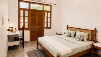 A bedroom with a bed, a desk, a chair, a ceiling fan, and a window with a wooden door.
