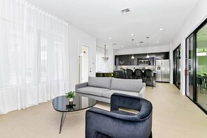 A modern living room with a grey sofa, a round glass coffee table, and a dark armchair. - Villa Domani 4BR - Private Pool - Near Disney (Davenport)